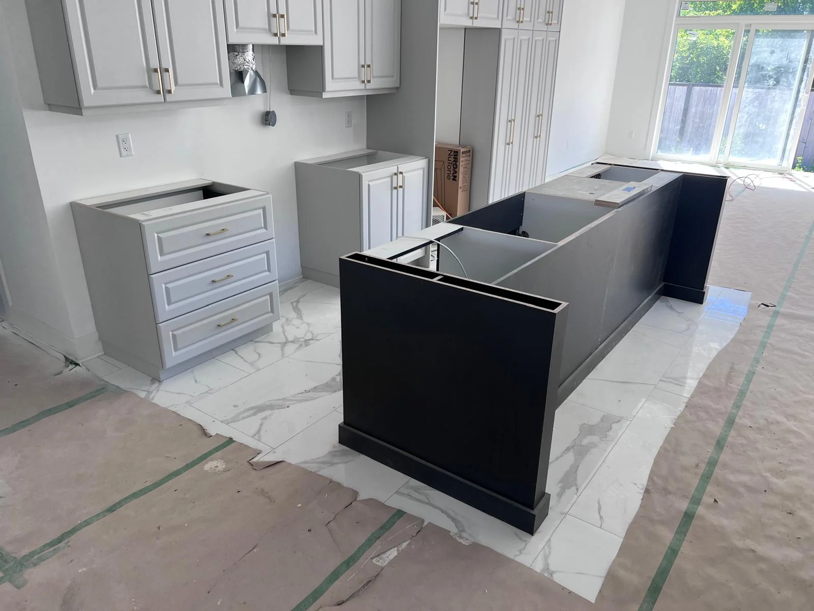 Project kitchen with white perimeter cabinets and a dark island, before countertops are installed.